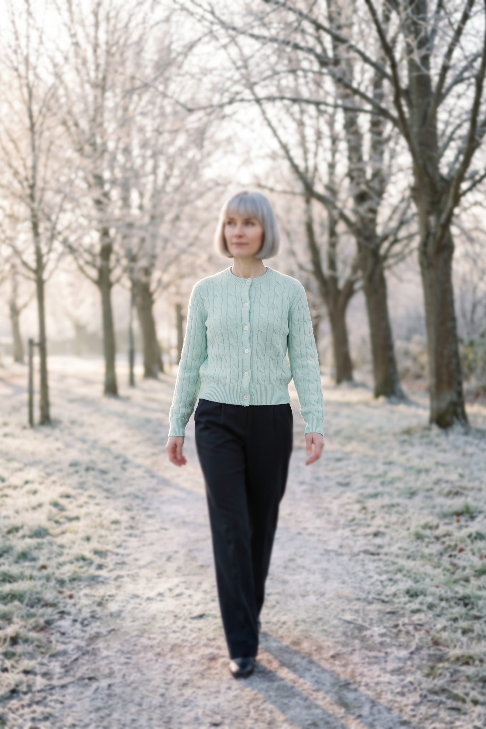 Woman in a mint-green cable-knit cardigan walking along a frosty park lane